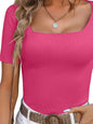 Woman wearing a pink top and white shorts against a textured wall.